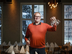 Mies seisoo viinilasit kädessään ravintolasalissa. Kuva Petteri Kivimäki