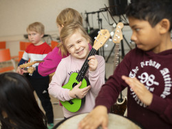 Tyttö soittaa vihreää kitaraa muiden oppilaiden keskellä / Hanna-Kaisa Hämäläinen